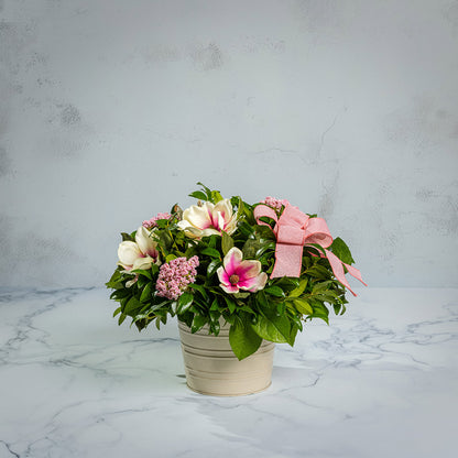 Fresh salal and green huckleberry with faux magnolia flowers, faux pink verbena, and a mauve pink bow in a white metal pot