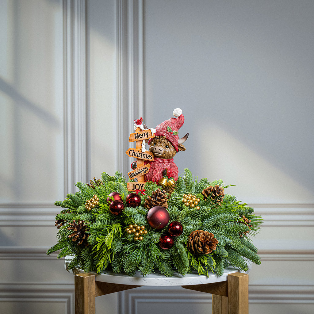 Decorative Christmas arrangement with a small bear figurine, ornaments, and a 'Merry Christmas' sign on a neutral background.