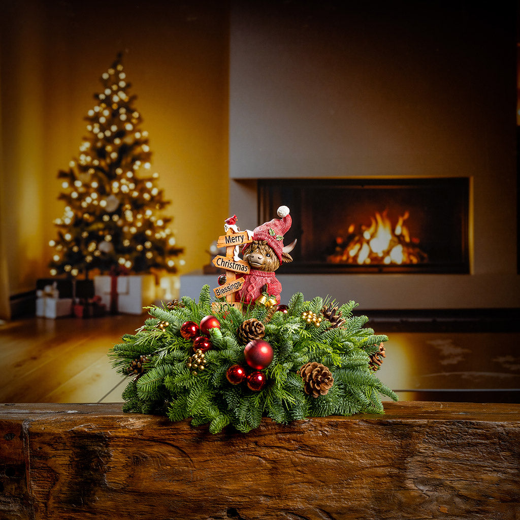 Decorative Christmas wreath with ornaments on a wooden surface, Christmas tree, and fireplace in the background.