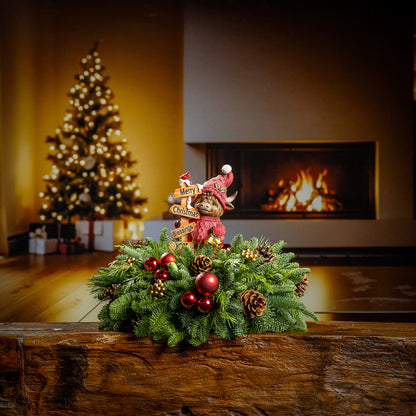 Decorative Christmas wreath with ornaments on a wooden surface, Christmas tree, and fireplace in the background.