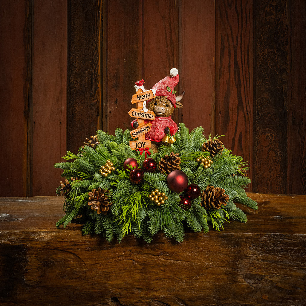 Decorative Christmas wreath with ornaments and a small bear figurine on a wooden surface.
