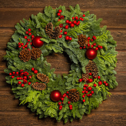 Christmas wreath with red berries, pine cones, and red balls on a wooden background
