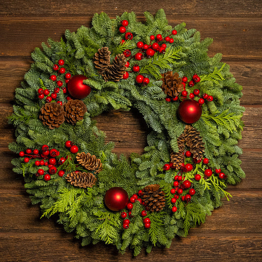 Christmas wreath with red berries, pine cones, and red balls on a wooden background
