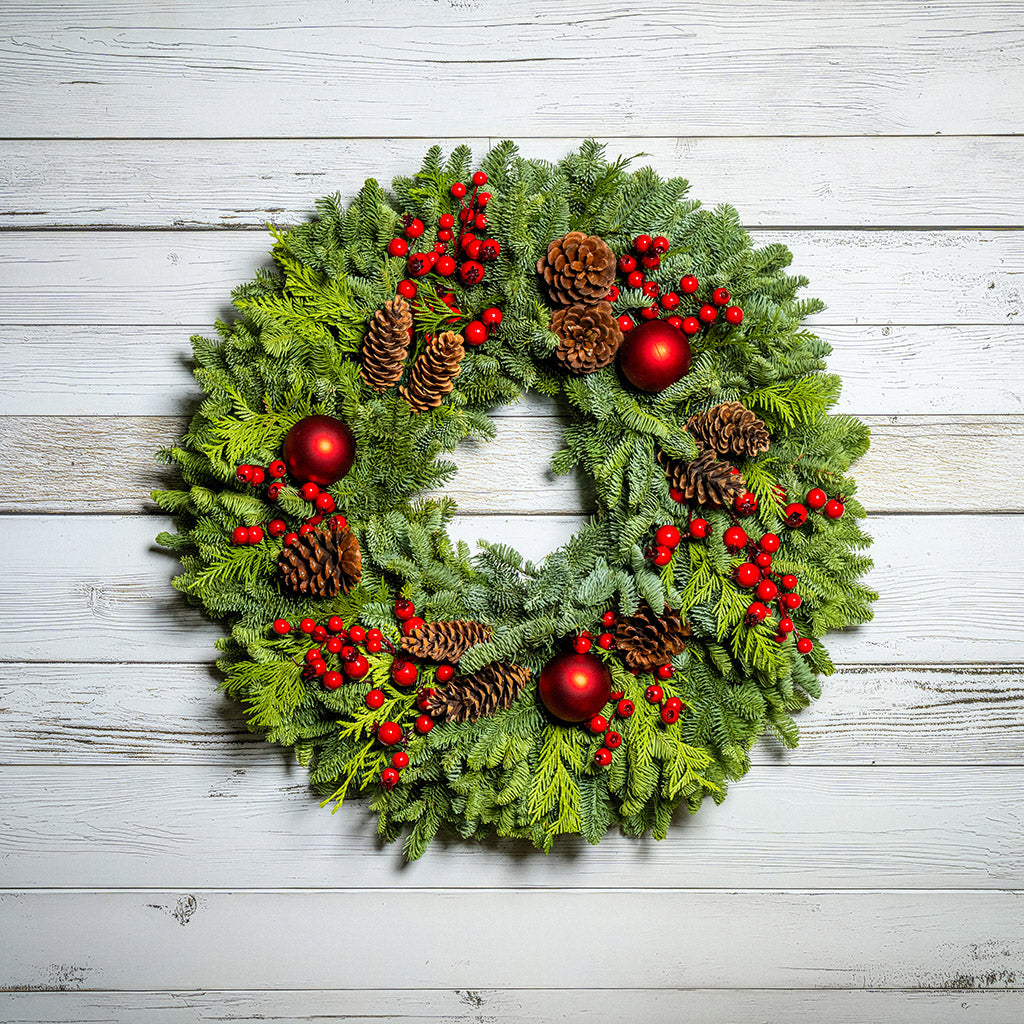 Christmas wreath with red berries, pine cones, and red balls on a wooden background