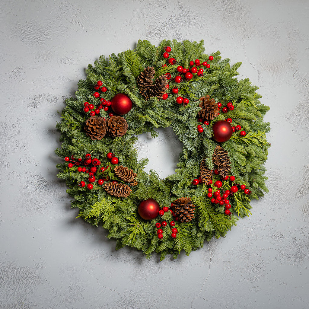 Christmas wreath with red berries, pine cones, and red balls on a light gray background