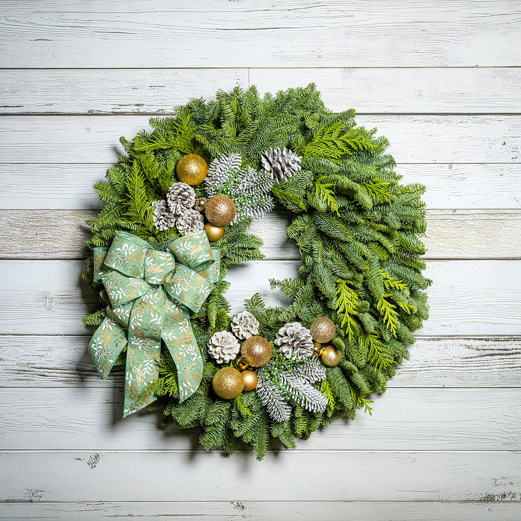 Christmas wreath with green bow, gold ornaments, and pine cones on a wooden background