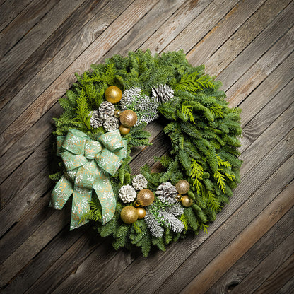 Decorative Christmas wreath with green bow, gold balls, and pinecones on a wooden background