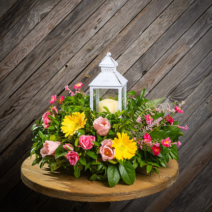 Fresh salal and green huckleberry with faux yellow gerbera daisies, faux mini pink roses, a mix of mini faux pink flowers, and faux tulips with a white LED lantern