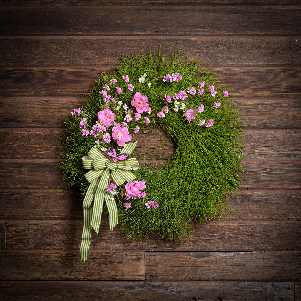 Green wreath with pink flowers and a green ribbon on a wooden background