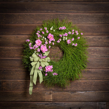 Green wreath with pink flowers and a green ribbon on a wooden background