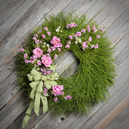 Floral wreath with pink flowers and a green bow on a wooden surface