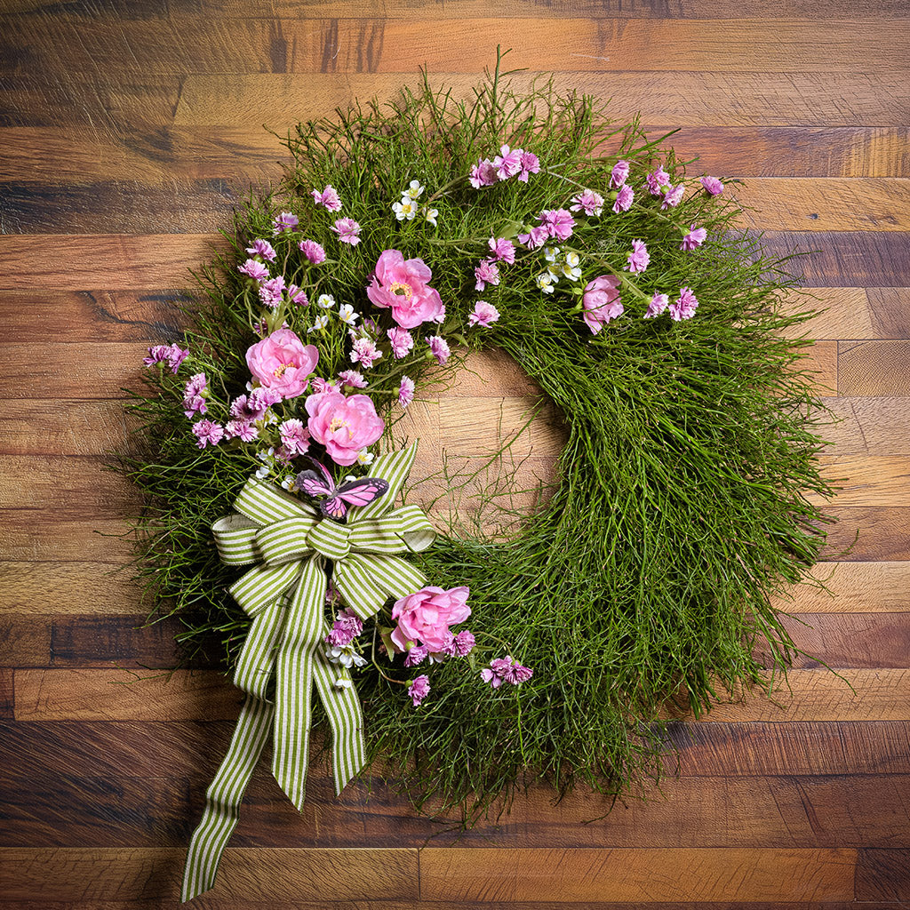 Green wreath with pink flowers and a green ribbon on a wooden background