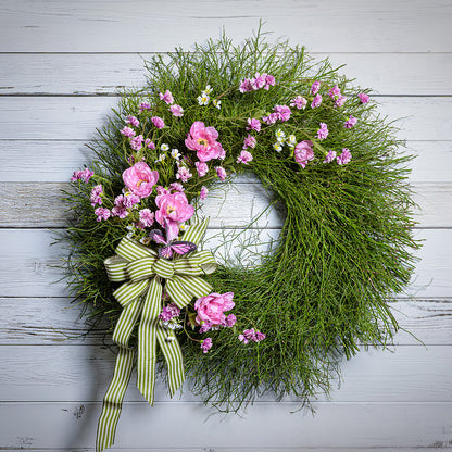 Floral wreath with pink flowers and a green bow on a wooden background