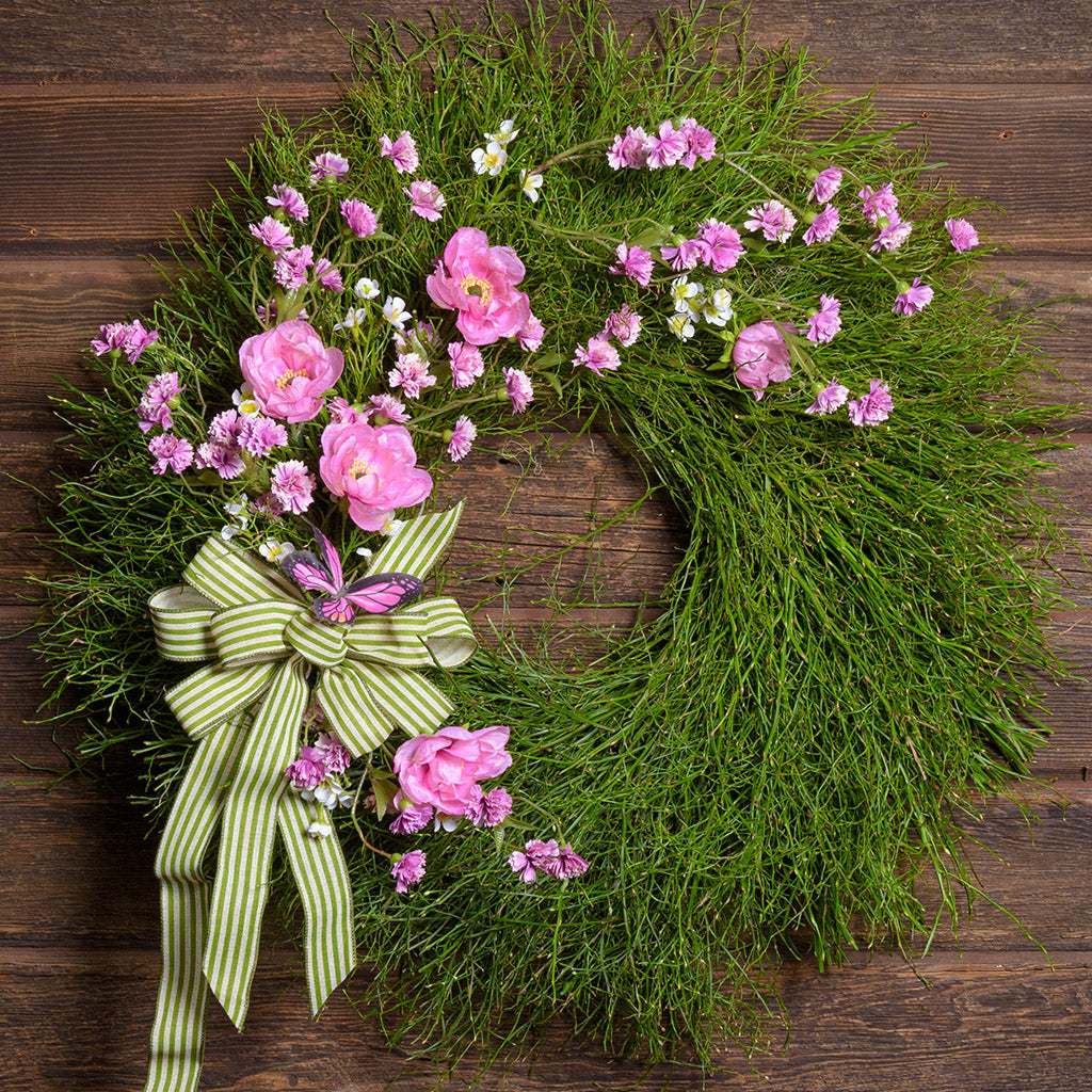 Wreath with pink flowers and a green bow on a wooden background