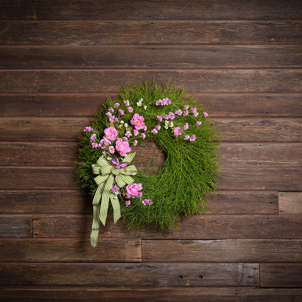 Green wreath with pink flowers and a green ribbon on a wooden background