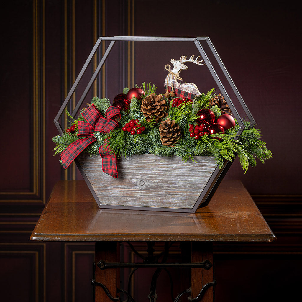 Decorative Christmas terrarium with greenery, ornaments, and a reindeer figure on a wooden surface.
