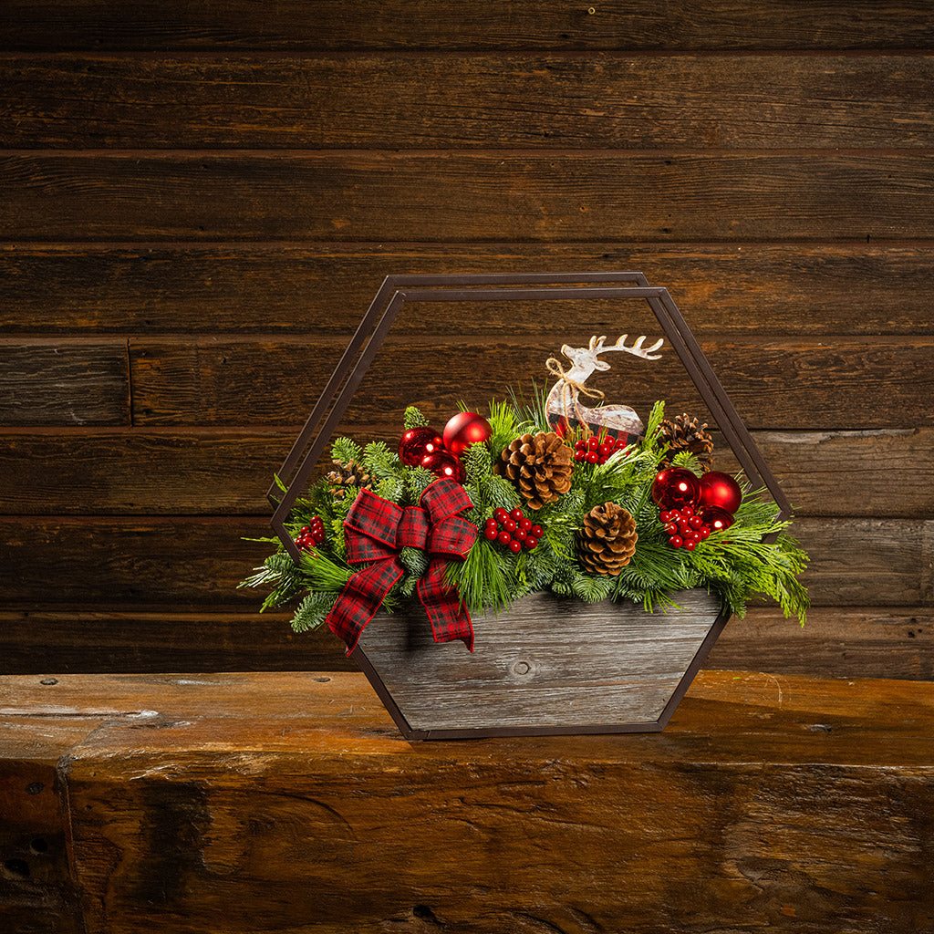 Decorative Christmas terrarium with greenery, red ornaments, and a reindeer figure on a wooden surface.