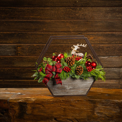 Decorative Christmas terrarium with greenery, red ornaments, and a reindeer figure on a wooden surface.