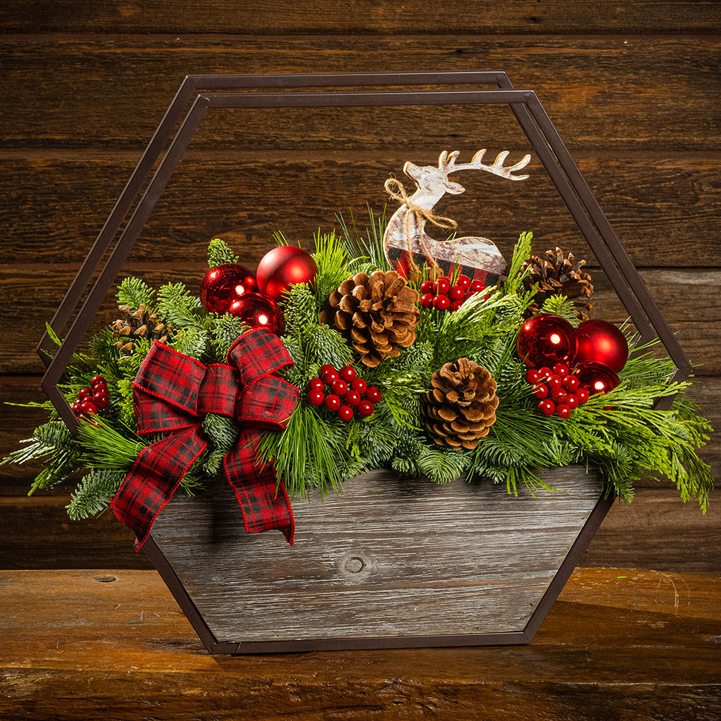 Decorative Christmas arrangement with greenery, red ornaments, and a reindeer figure on a wooden background.