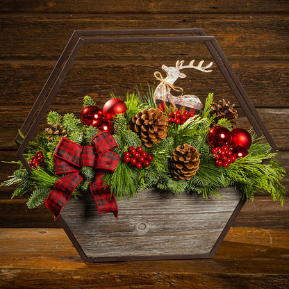 Decorative Christmas arrangement with greenery, red ornaments, and a reindeer figure on a wooden background.