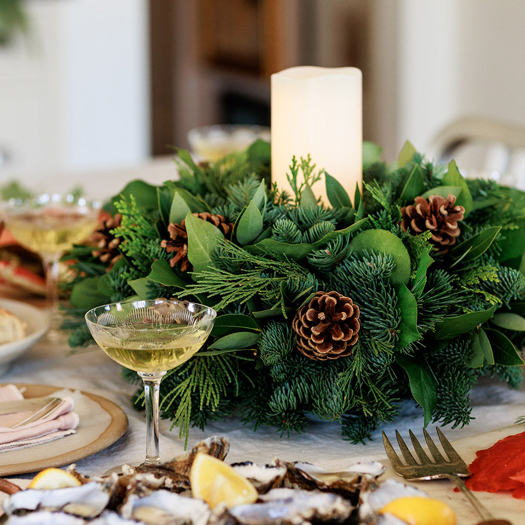 An arrangement of noble fir, cedar, white pine, salal, bay leaves, pinecones, and an ivory LED candle 