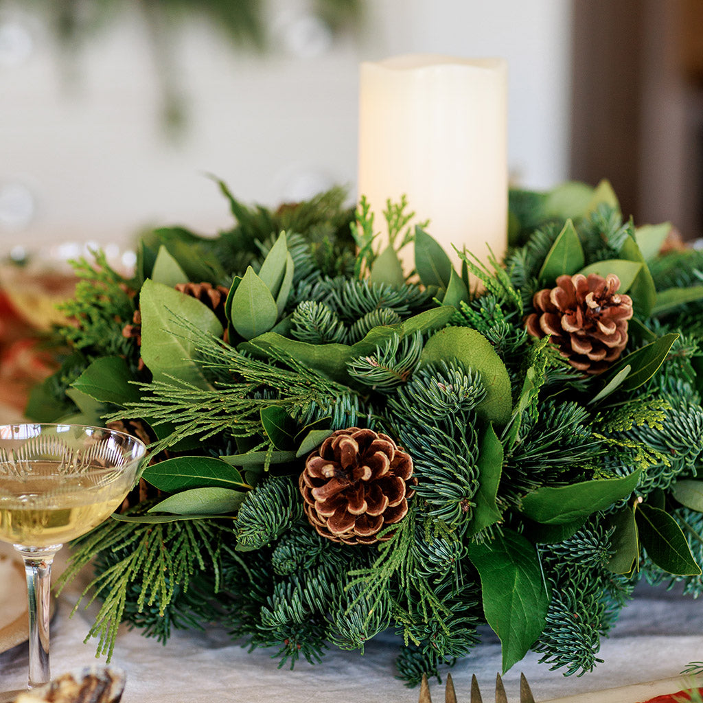 An arrangement of noble fir, cedar, white pine, salal, bay leaves, pinecones, and an ivory LED candle 