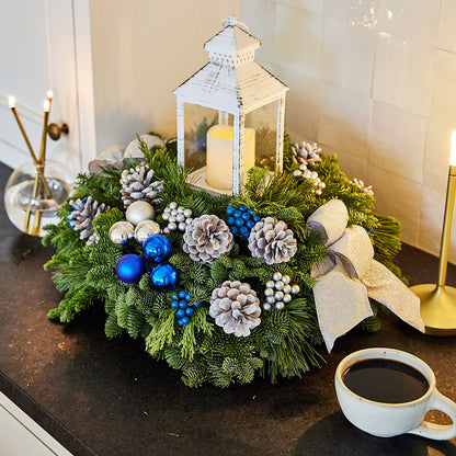 Evergreen centerpiece with white pine cones, silver and blueberries and balls, silver glitter bow and a white LED lantern