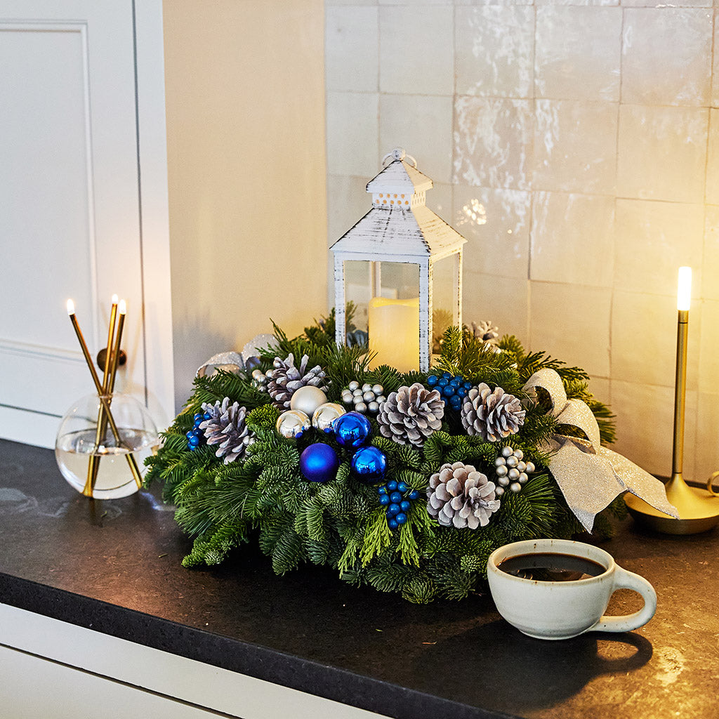 Evergreen centerpiece with white pine cones, silver and blueberries and balls, silver glitter bow and a white LED lantern