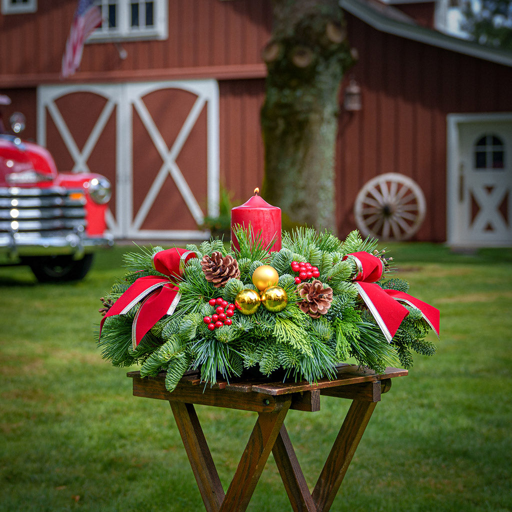 Centerpiece with pine cones, gold balls, red berry clusters,gold trimmed red bow tucks and a red pillar candle