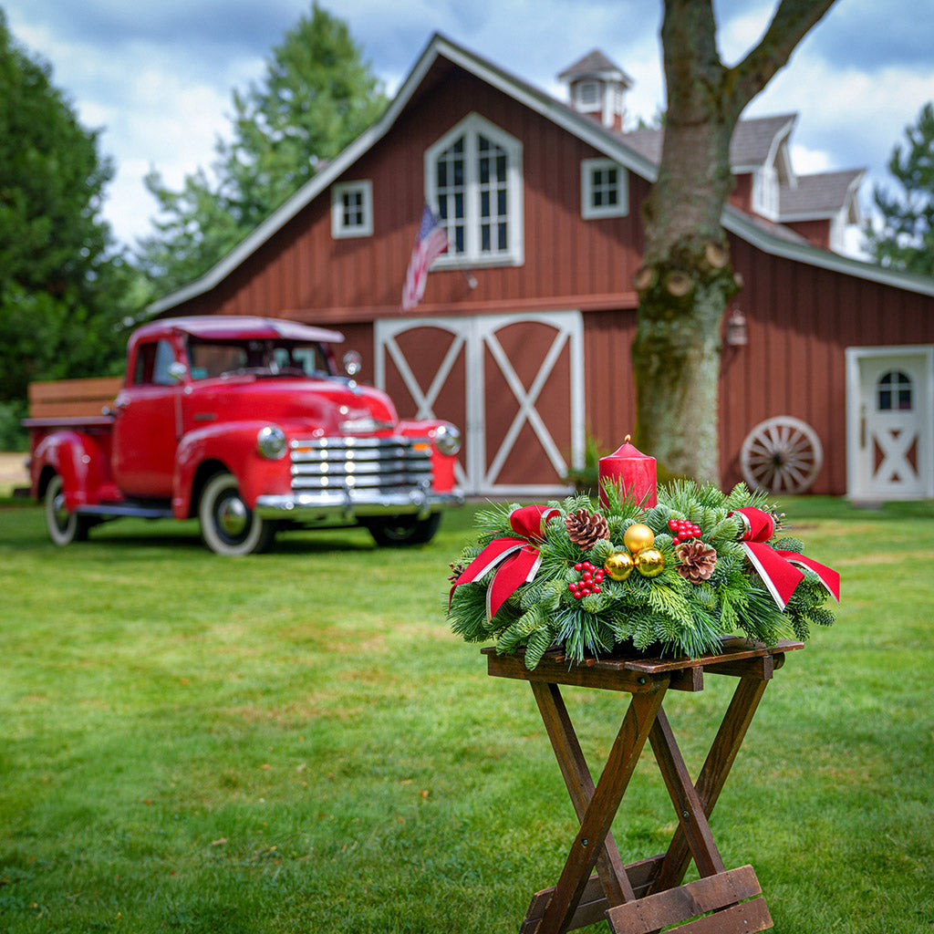 Centerpiece with pine cones, gold balls, red berry clusters,gold trimmed red bow tucks and a red pillar candle