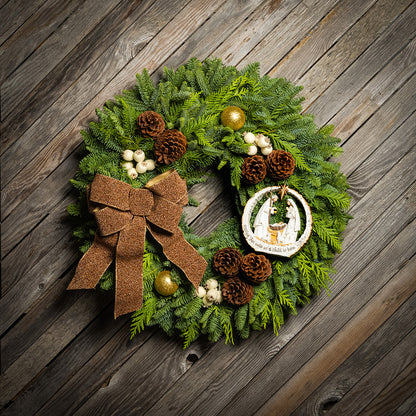 Christmas wreath with greenery, pinecones, and a brown bow on a wooden background