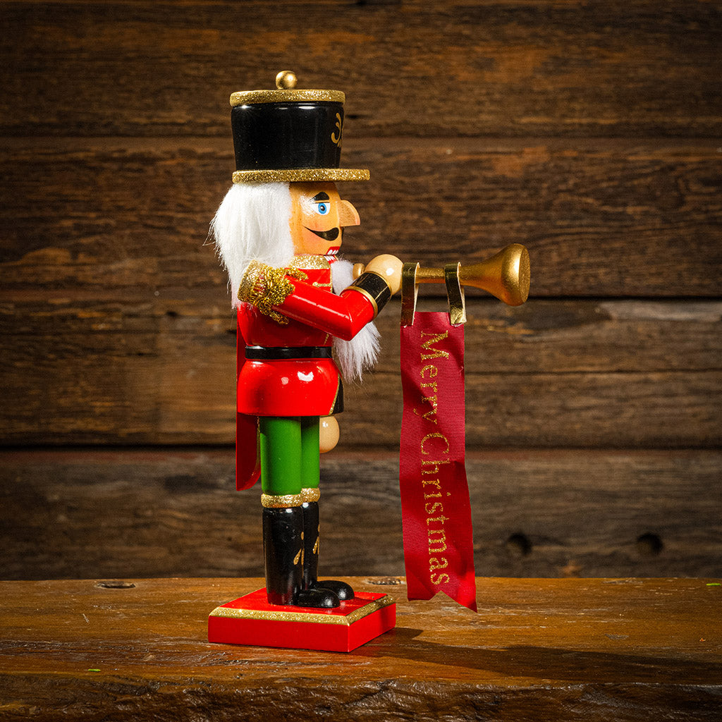 Wooden nutcracker holding bugle with a red merry Christmas banner.