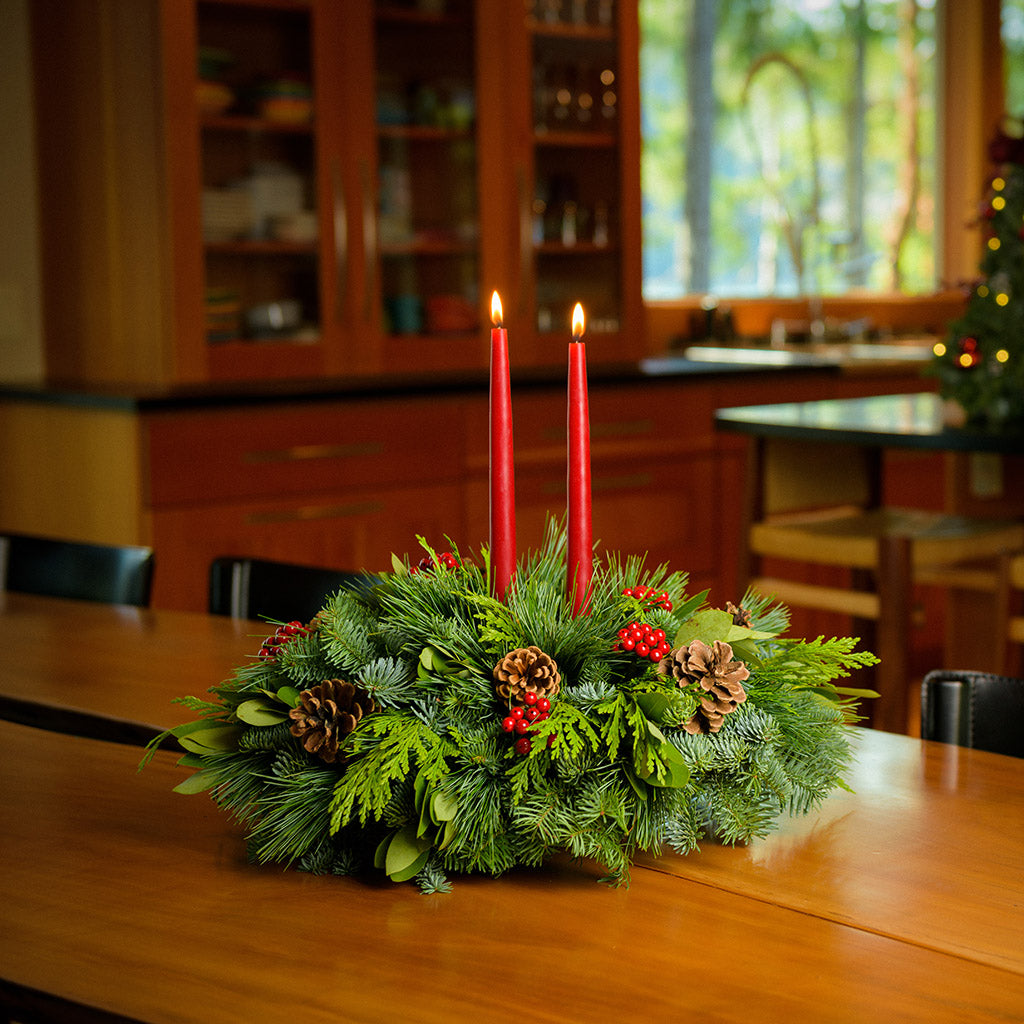 Centerpiece made of noble fir, pine, incense cedar and bay leaves with egg-sized ponderosa pine cones, red berry clusters, and 2 red 12" taper candles