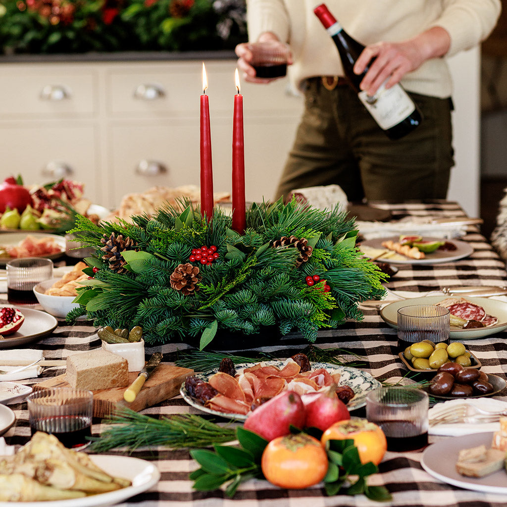 Centerpiece made of noble fir, pine, incense cedar and bay leaves with egg-sized ponderosa pine cones, red berry clusters, and 2 red 12" taper candles