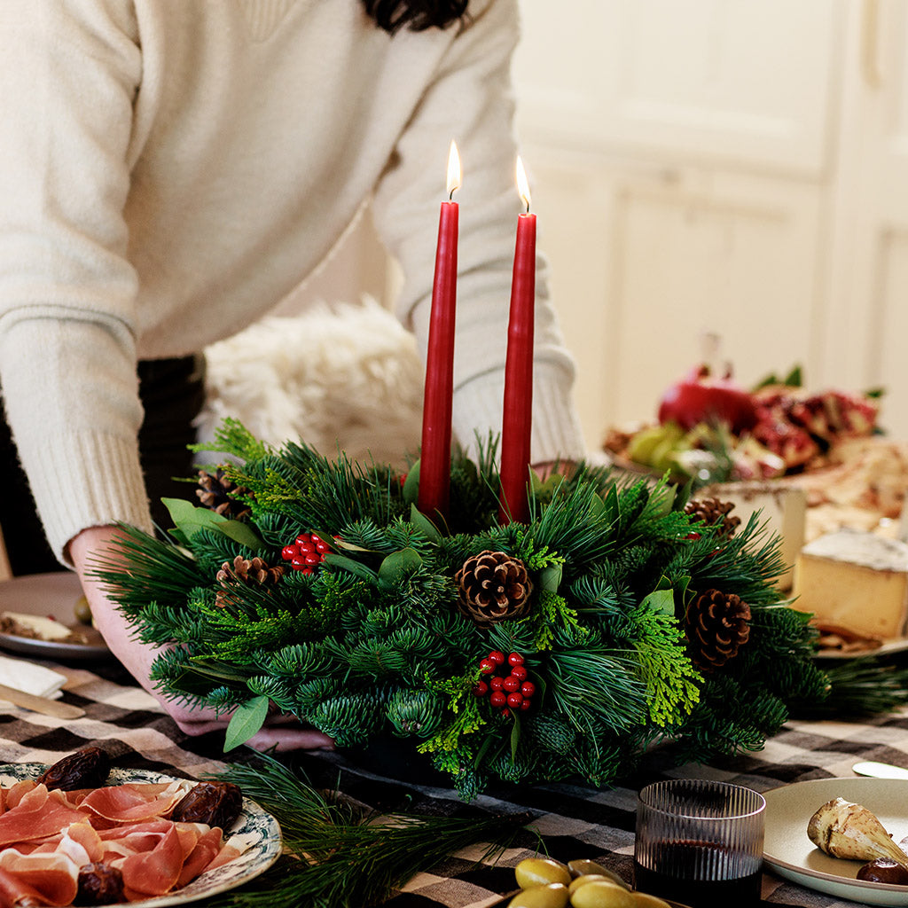 Centerpiece made of noble fir, pine, incense cedar and bay leaves with egg-sized ponderosa pine cones, red berry clusters, and 2 red 12" taper candles