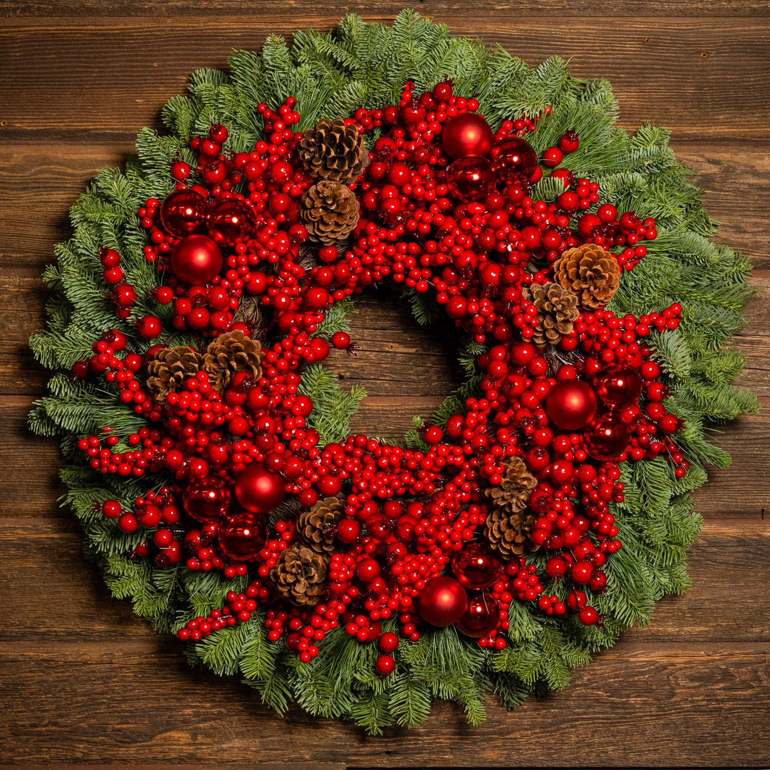 Christmas wreath made of noble fir and white pine with a ring of faux red pepperberries, red ball clusters, and white-pine cones