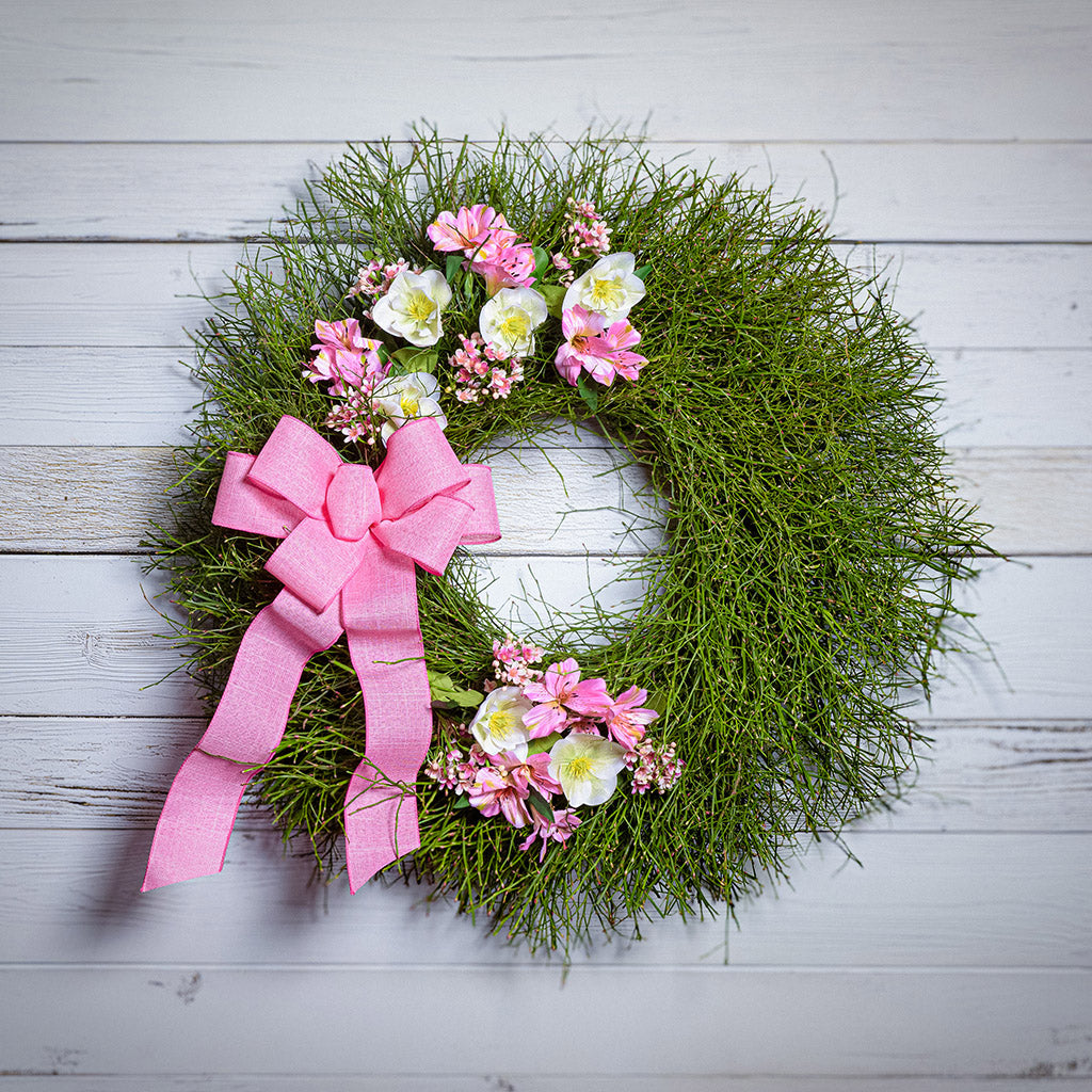Green wreath with pink and white flowers and a pink bow on a light wooden background