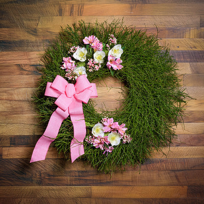 Green wreath with pink flowers and a pink bow on a wooden surface