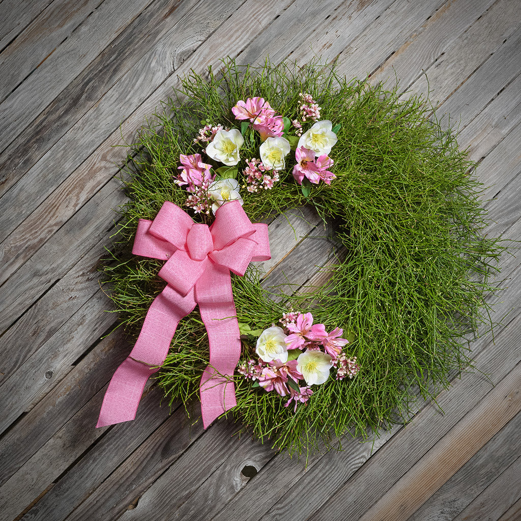 Wreath with pink flowers and a large pink bow on a wooden surface