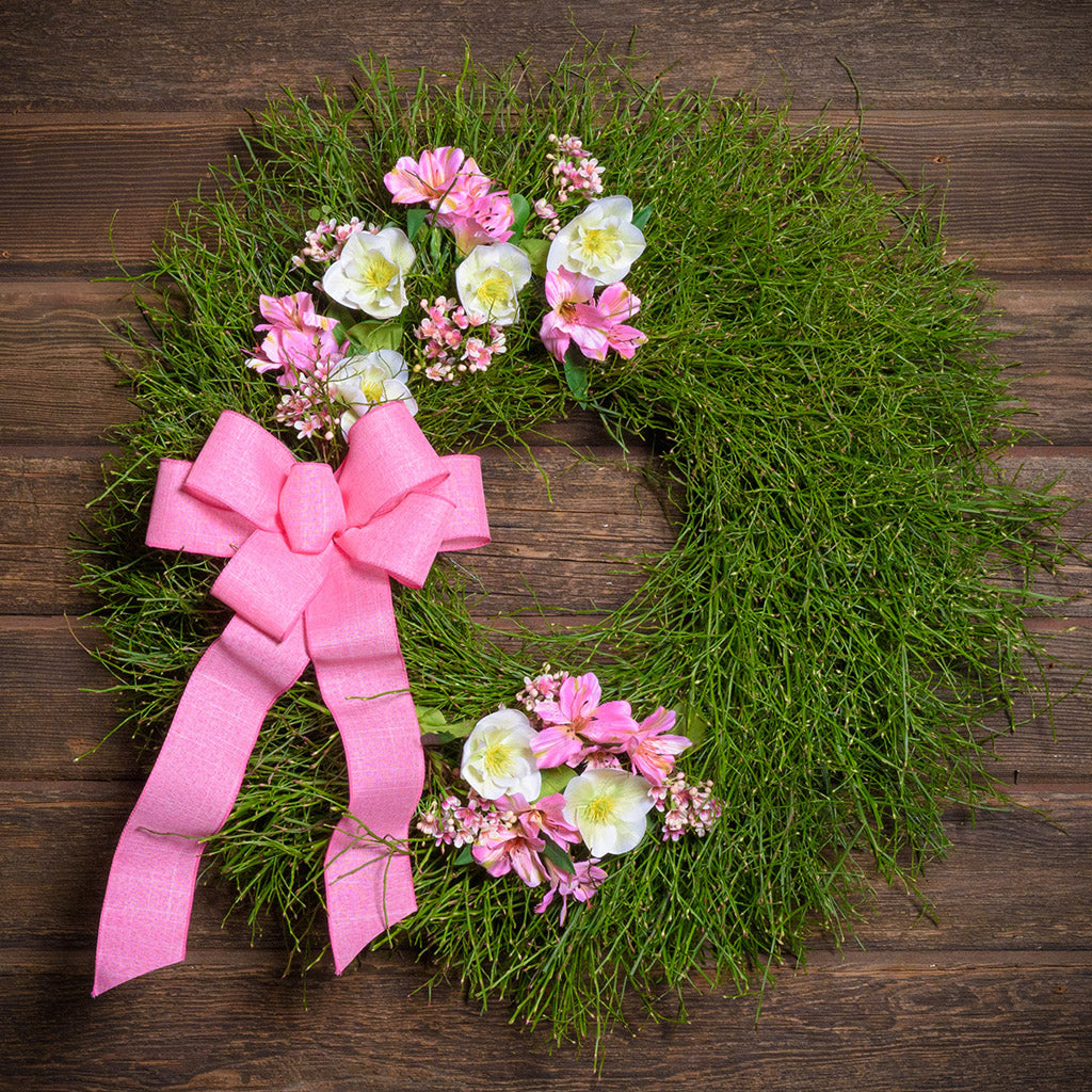 Green wreath with pink flowers and a pink bow on a wooden background