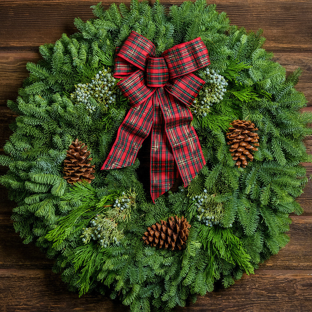 Christmas wreath of noble, cedar, juniper, pine cones and a red plaid bow close up