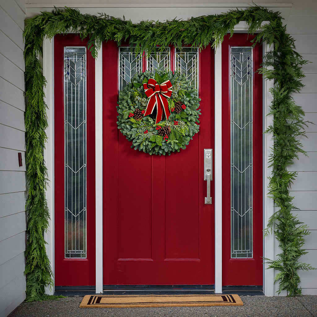 Christmas wreath of noble, cedar, juniper and salal with pine cones, red bow with gold edges and red berry clusters