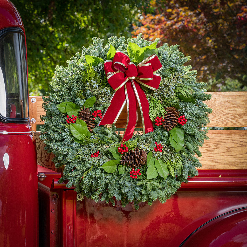 Christmas wreath of noble, cedar, juniper and salal with pine cones, red bow with gold edges and red berry clusters