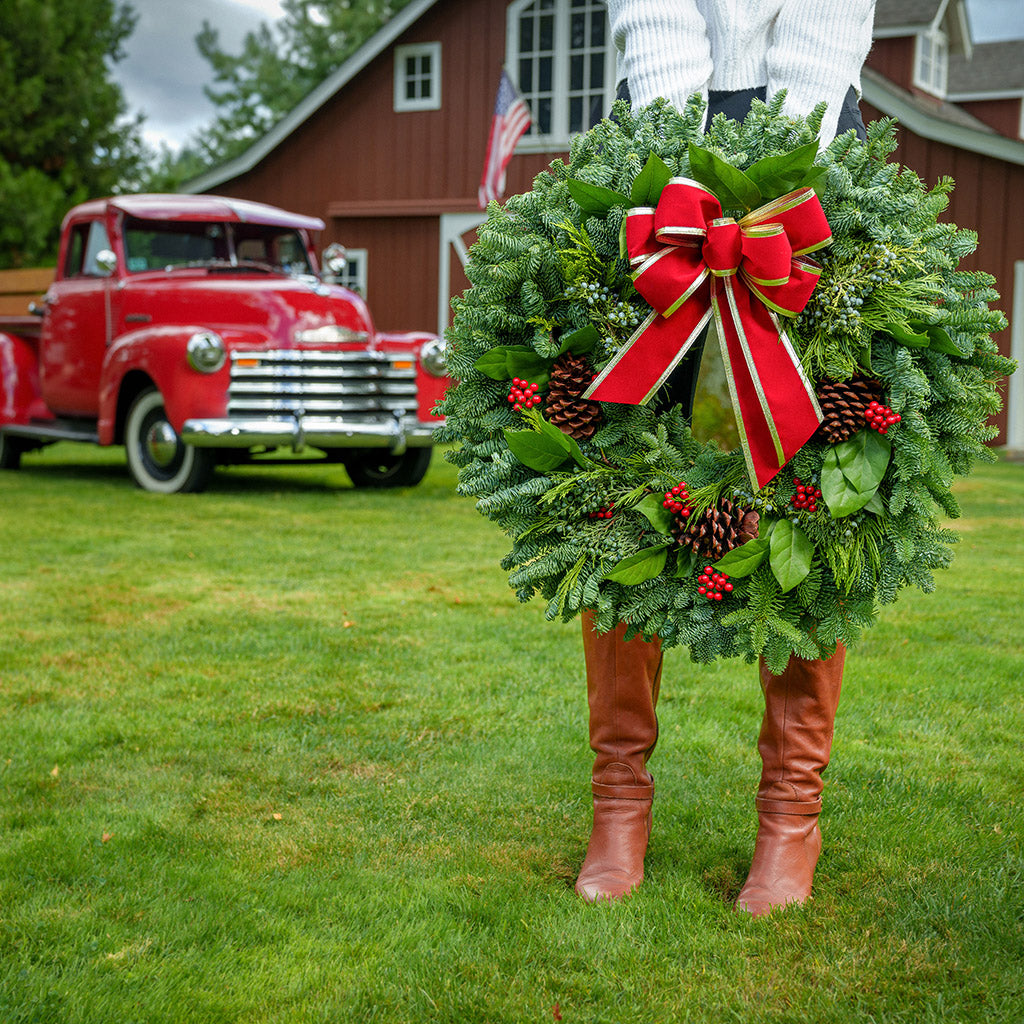 Christmas wreath of noble, cedar, juniper and salal with pine cones, red bow with gold edges and red berry clusters