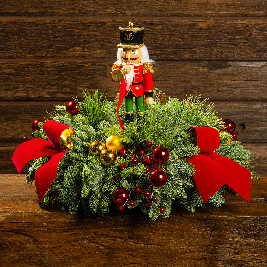 greenery with red and gold ball ornaments, faux red berry branches, red velvet bows, and a wooden bugler Nutcracker decoration with a wooden background.