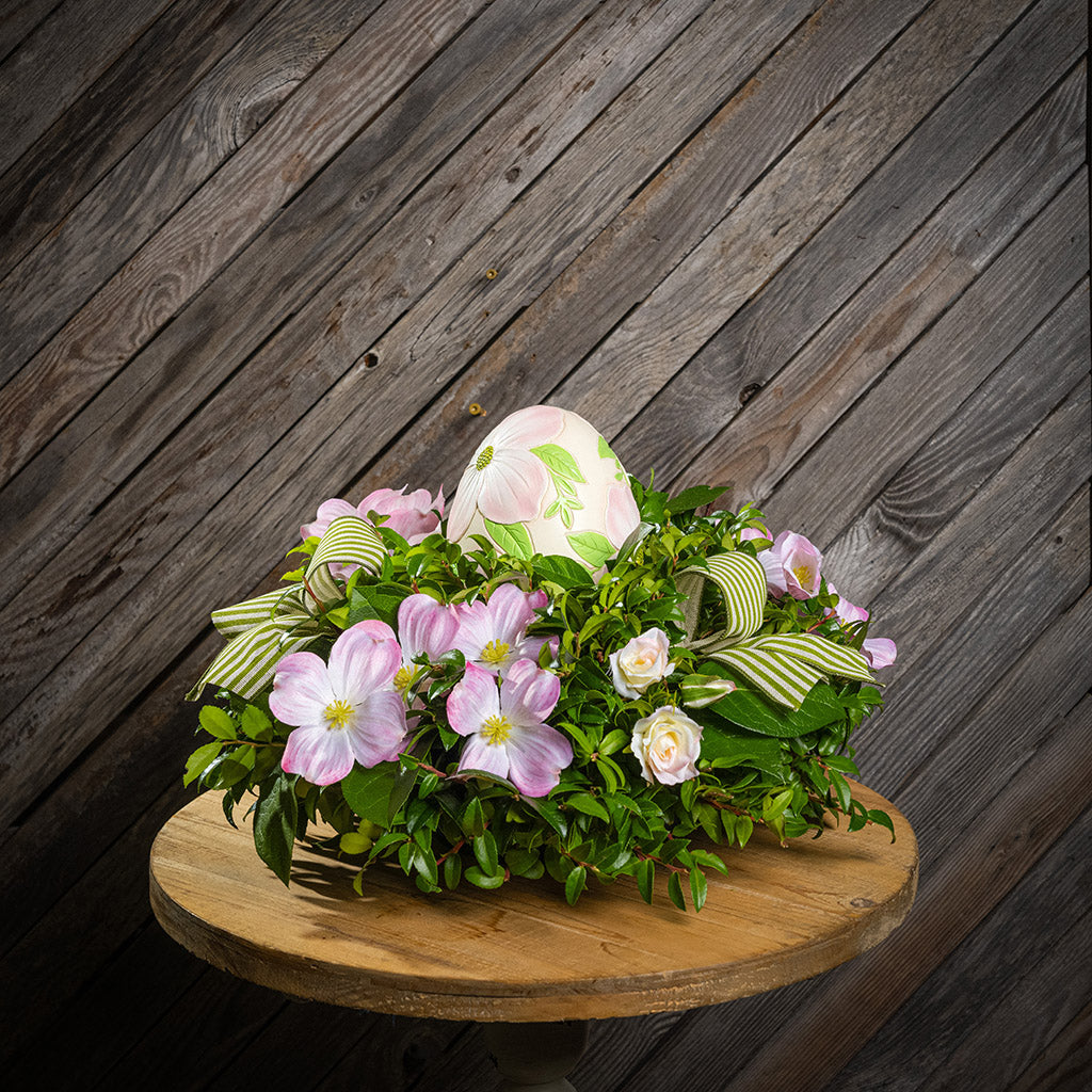 Fresh salal and green huckleberry with faux dogwood flowers, faux pink blush roses, green and ivory striped bows, and a decorative resin egg etched with dogwood flowers