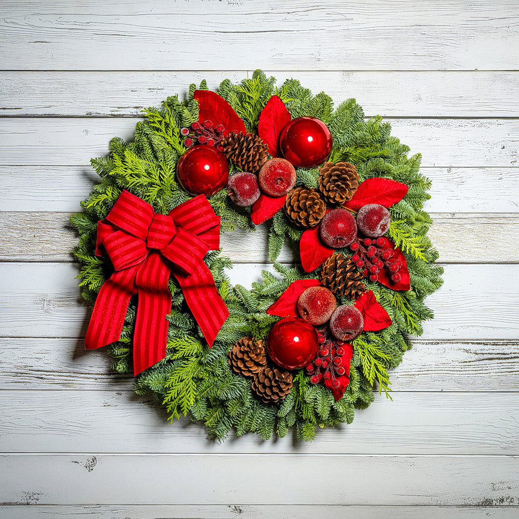 Christmas wreath with red bow, berries, and pine cones on a wooden background