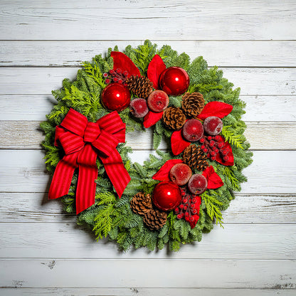 Christmas wreath with red bow, berries, and pine cones on a wooden background