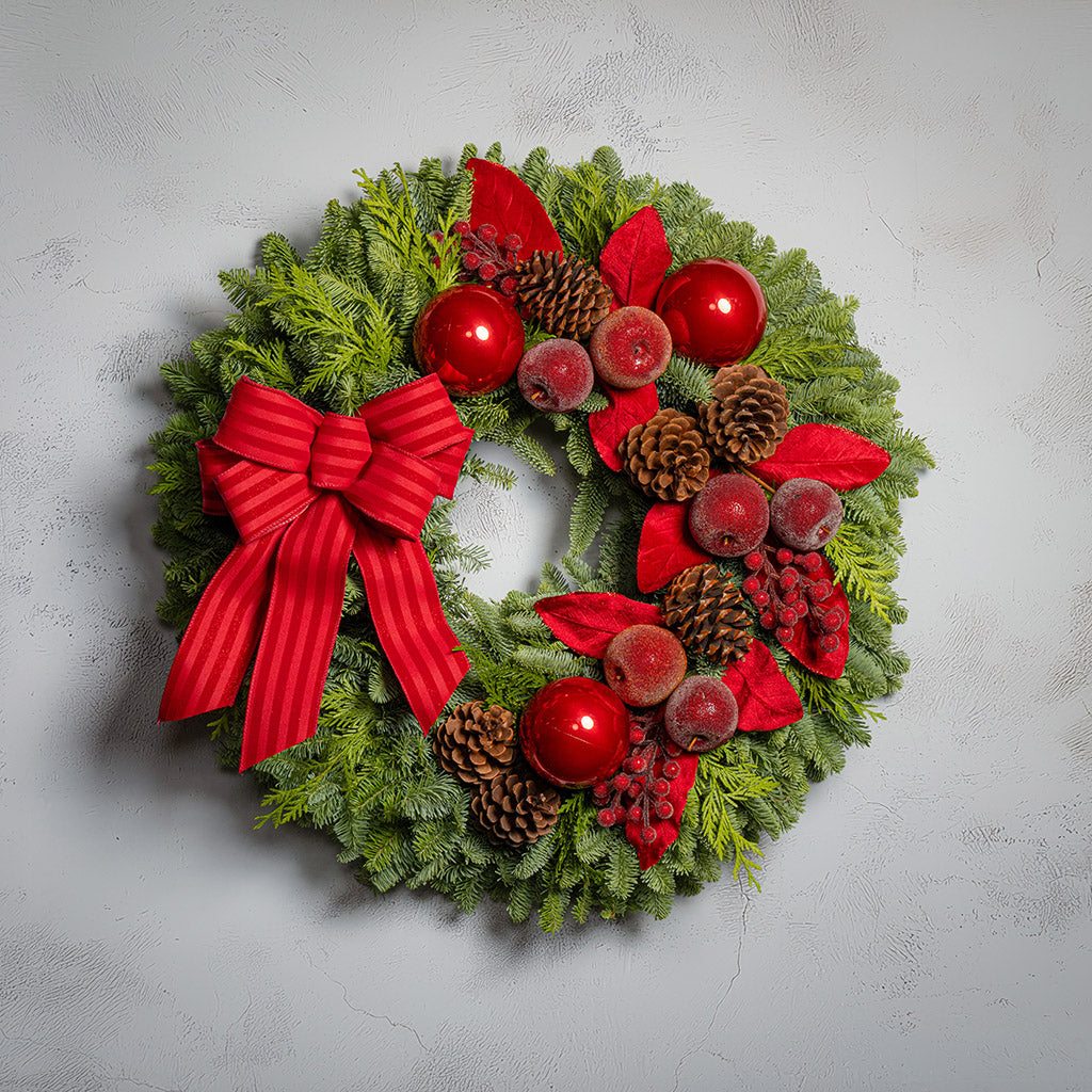 Christmas wreath with red bow, berries, and pinecones on a light gray background