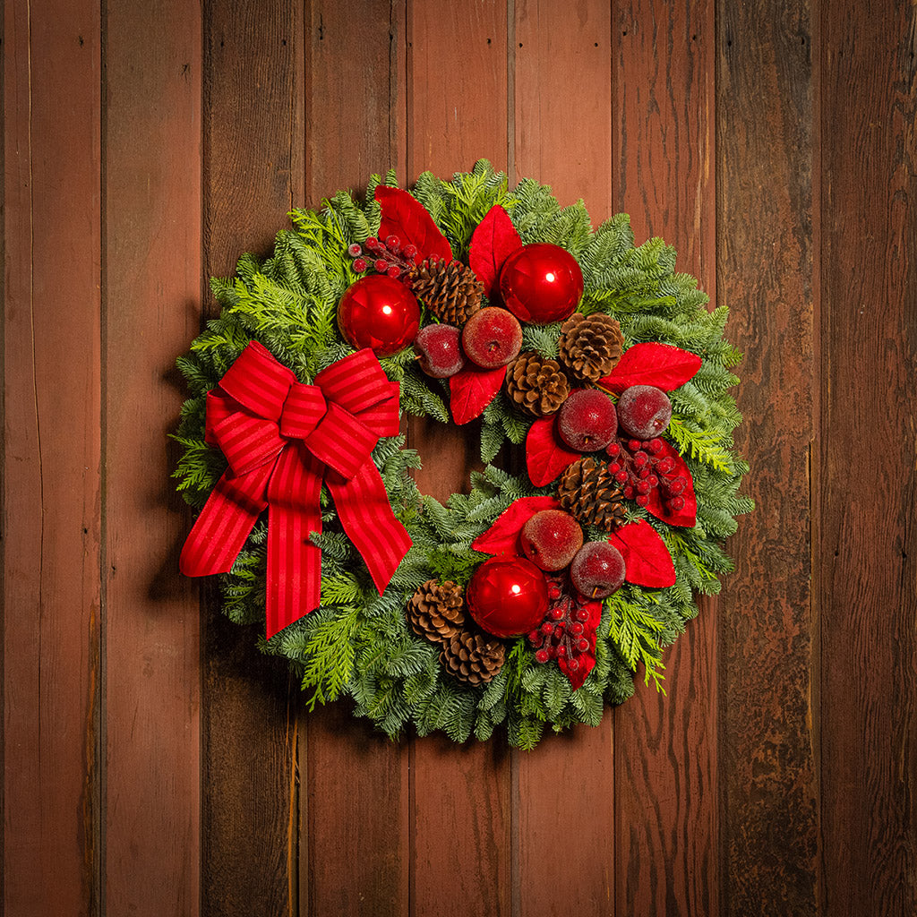 Christmas wreath with red berries, pine cones, and a large red bow on a wooden door.